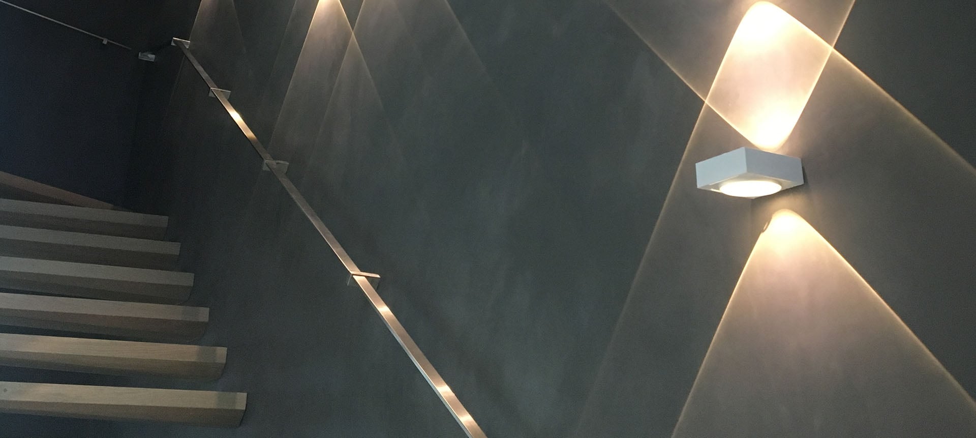 Montée d'escalier en enduit à la chaux noir et marches en béton ciré, éclairage rasant — réalisation Arts des Matières en Alsace